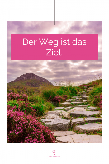 Weg aus Steinplatten mit viel Grün, Berg und rosa Blumen. Zitat-Text: "Der Weg ist das Ziel."